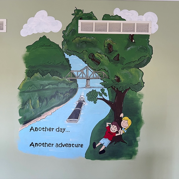 A colorful mural depicting two children hanging from a tree, enjoying a river view with the caption "Another day... Another adventure."
